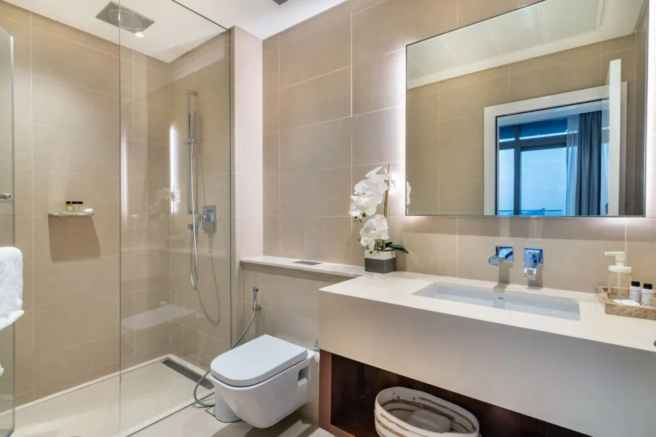 A tiled bathroom with a glass shower, toilet, and long vanity.