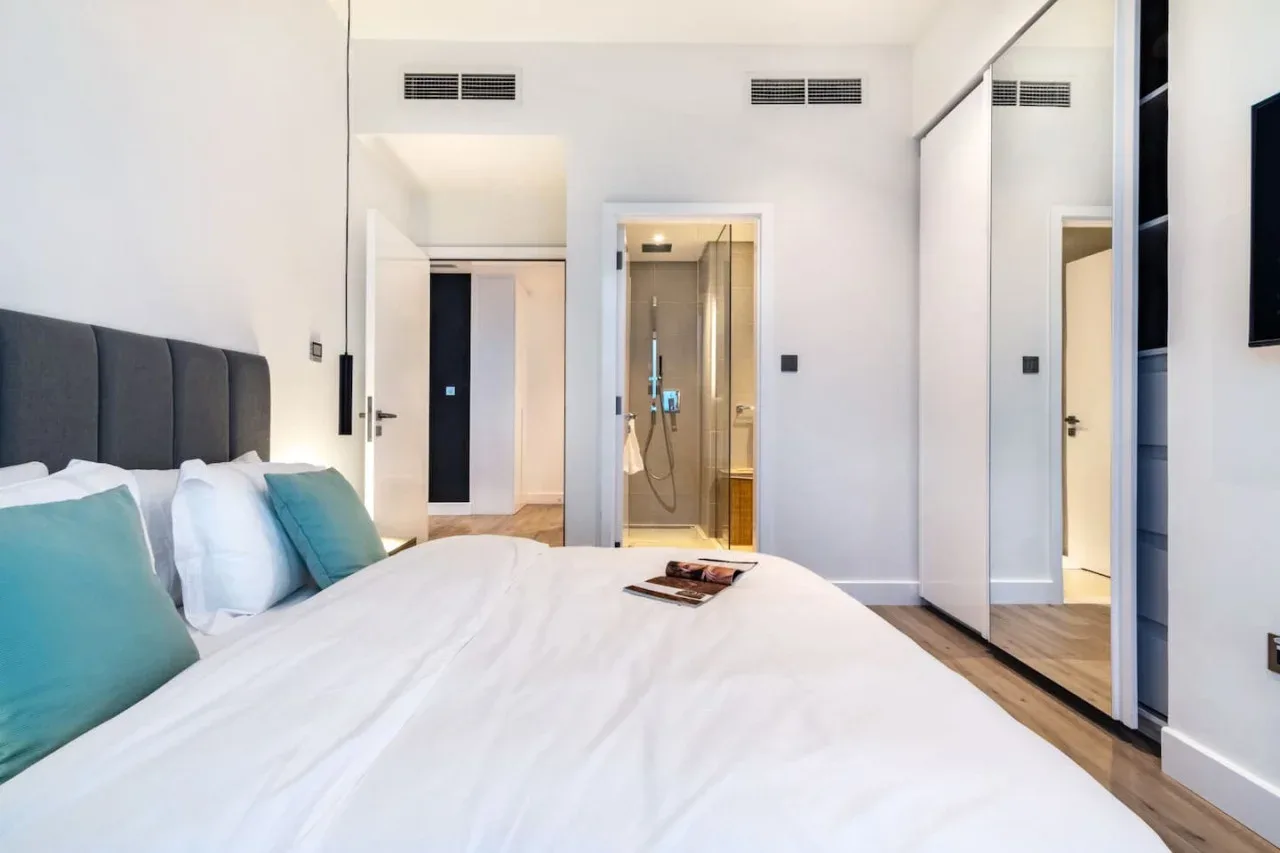 A bright bedroom with a bed facing an open bathroom shower.