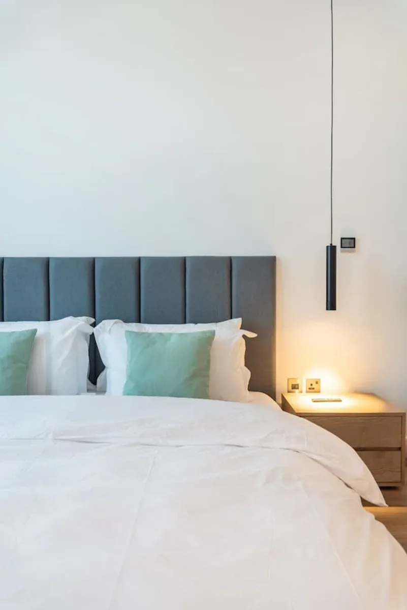 A bedroom with a neatly made bed and a tall upholstered headboard.