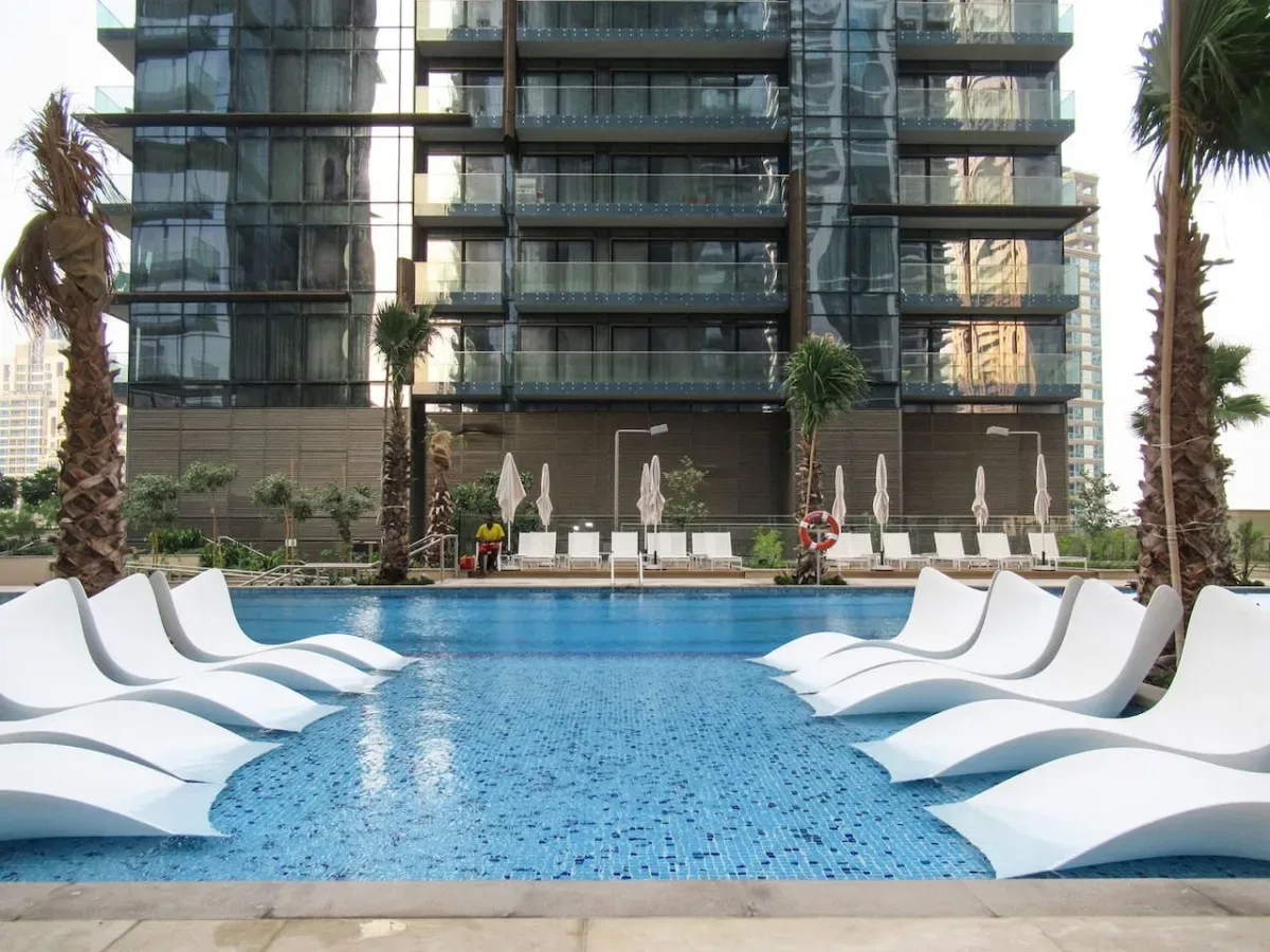 Piscina al aire libre con tumbonas blancas junto a un edificio moderno.