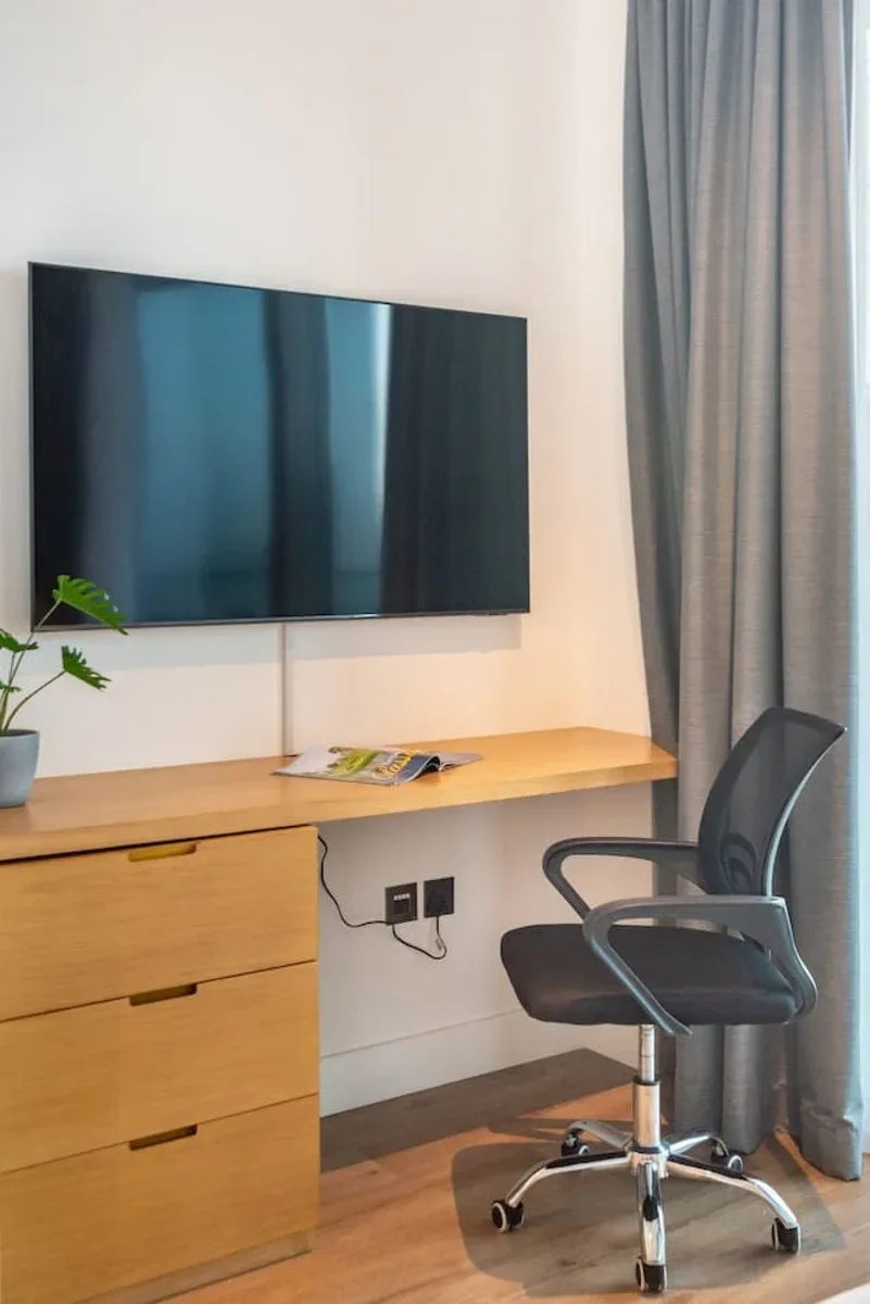 A room with a wall-mounted television, wooden desk, and office chair.