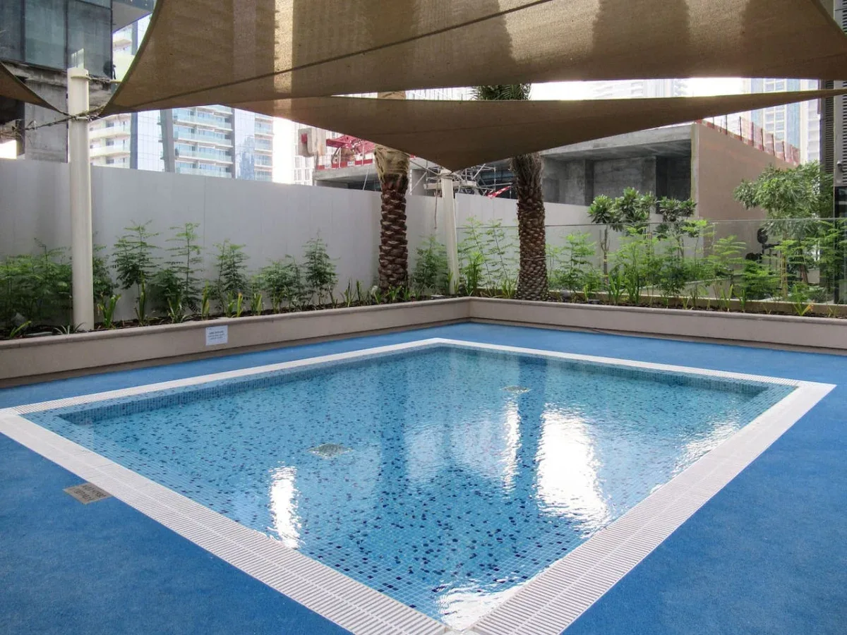 An outdoor swimming pool sits beneath shade sails, with plants along the surrounding wall.