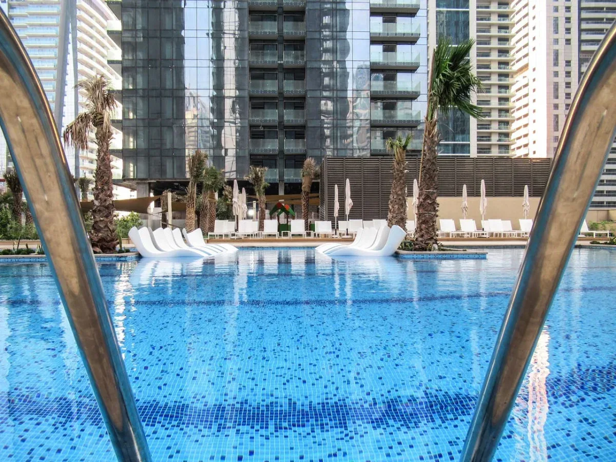 An outdoor swimming pool is framed by curved metal rails and tall buildings.