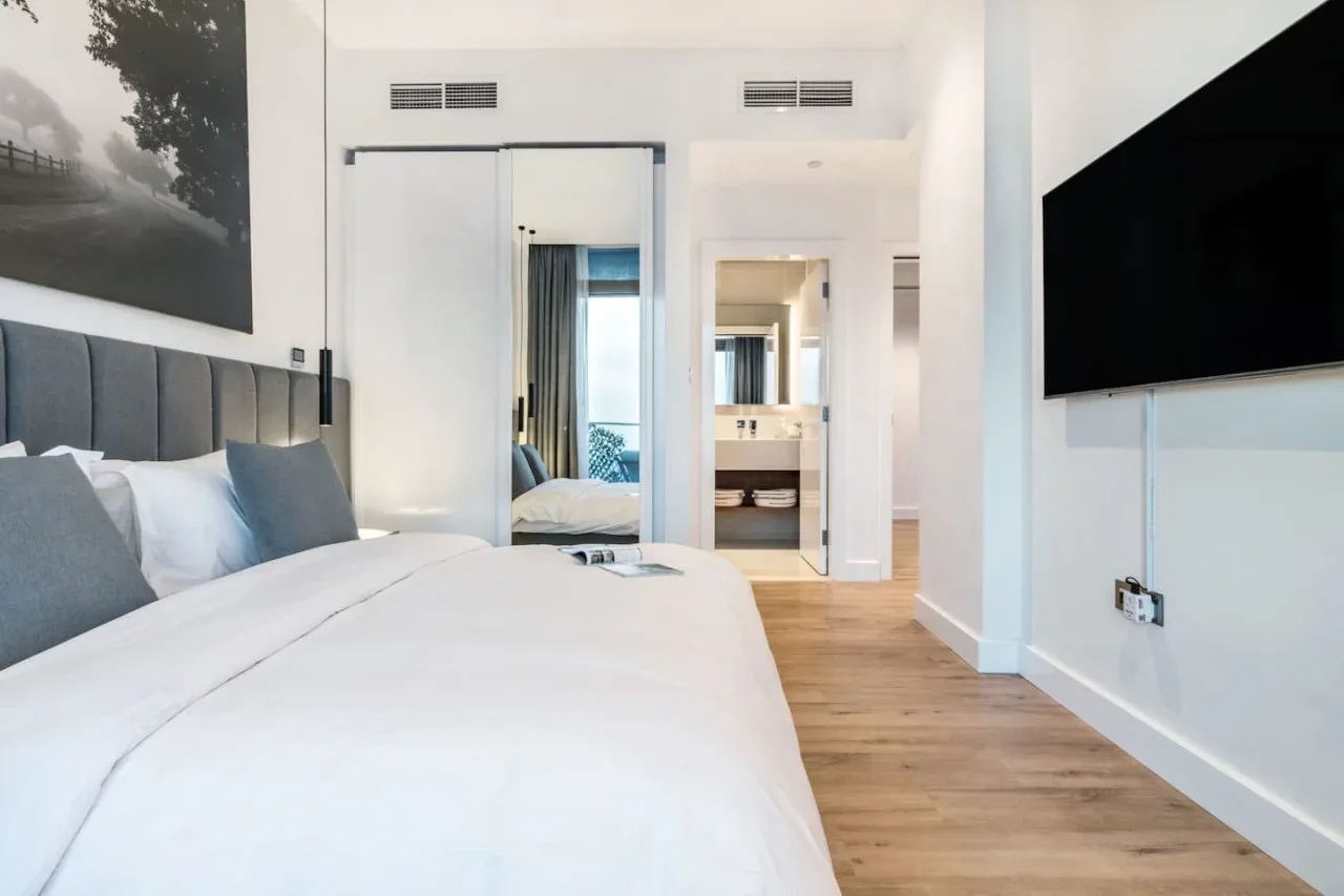 A bright bedroom with a white bed and a television mounted on the wall.
