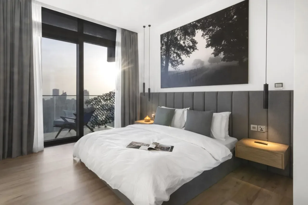 A bright bedroom with a large bed, gray headboard, and glass doors.