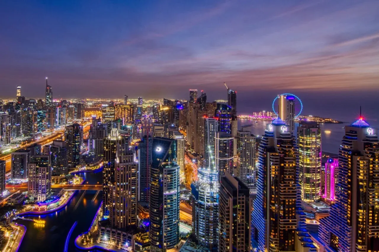 City skyline at dusk with illuminated skyscrapers and a waterfront.