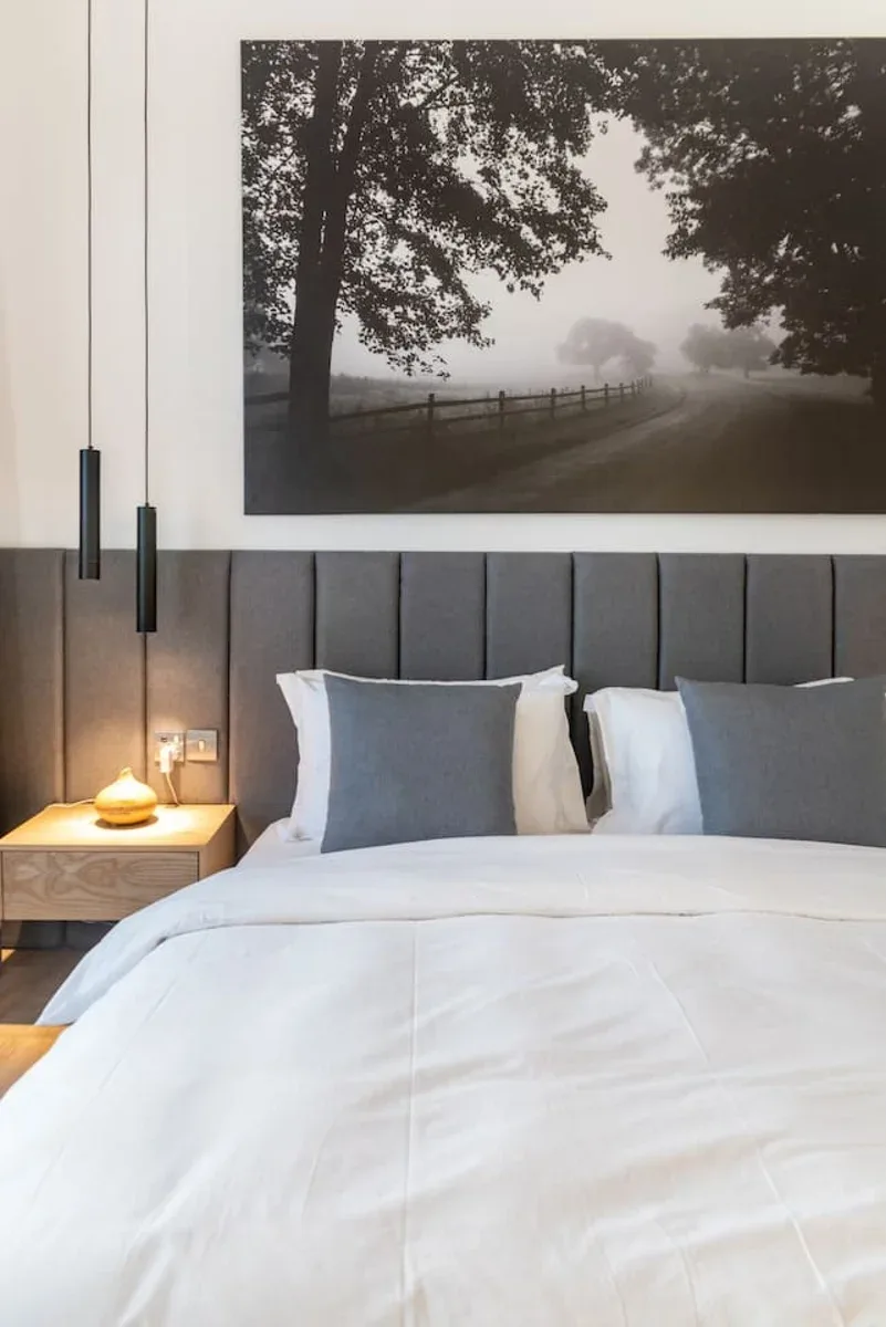 A bedroom with a neatly made bed beneath a large black-and-white landscape photograph.