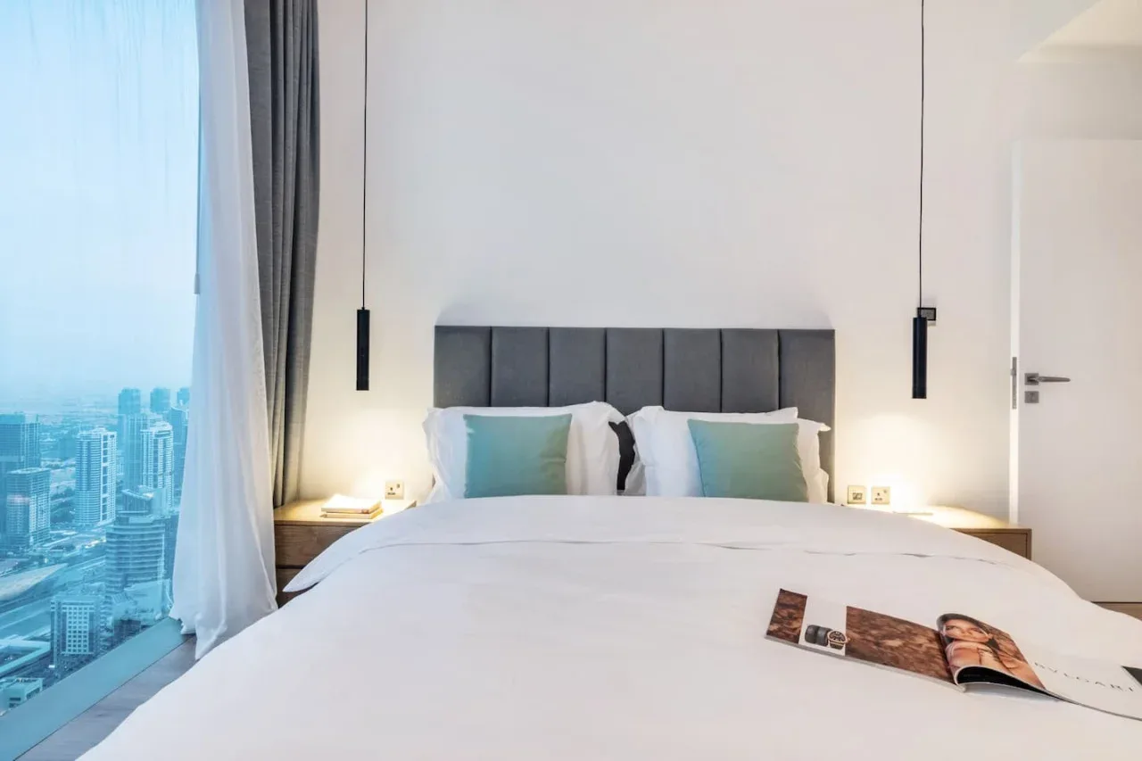 A bedroom with a neatly made bed and a city view through the window.