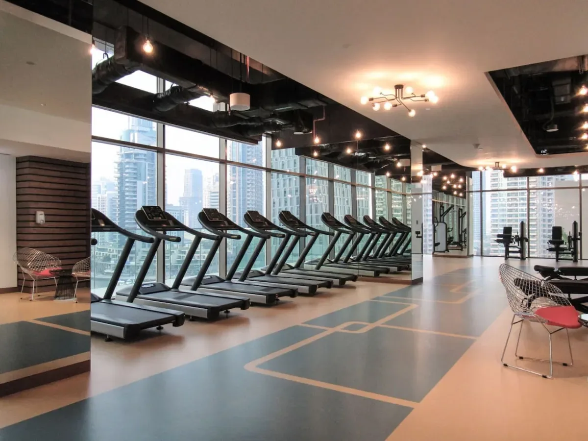 Un gimnasio con cintas de correr y equipo de ejercicio junto a grandes ventanales.