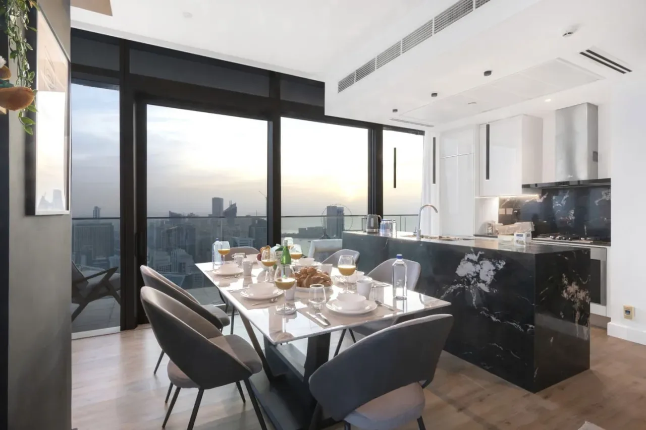A dining area with a set table beside large windows and an open kitchen.