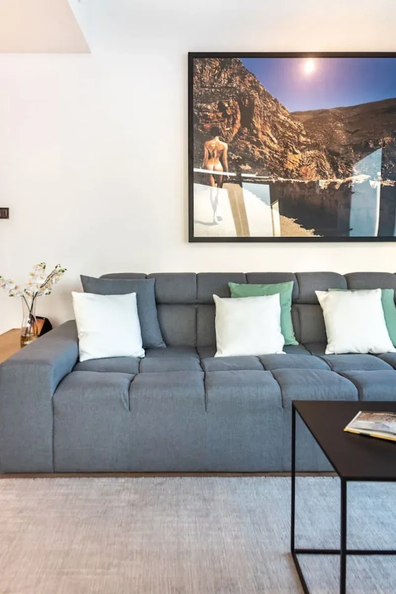 A living room with gray seating beneath a large landscape picture.
