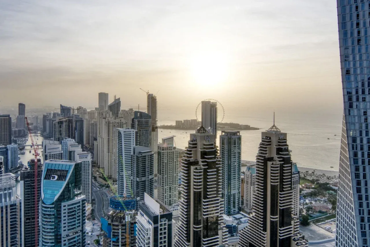 A city skyline of high-rise buildings overlooks the water at sunset.