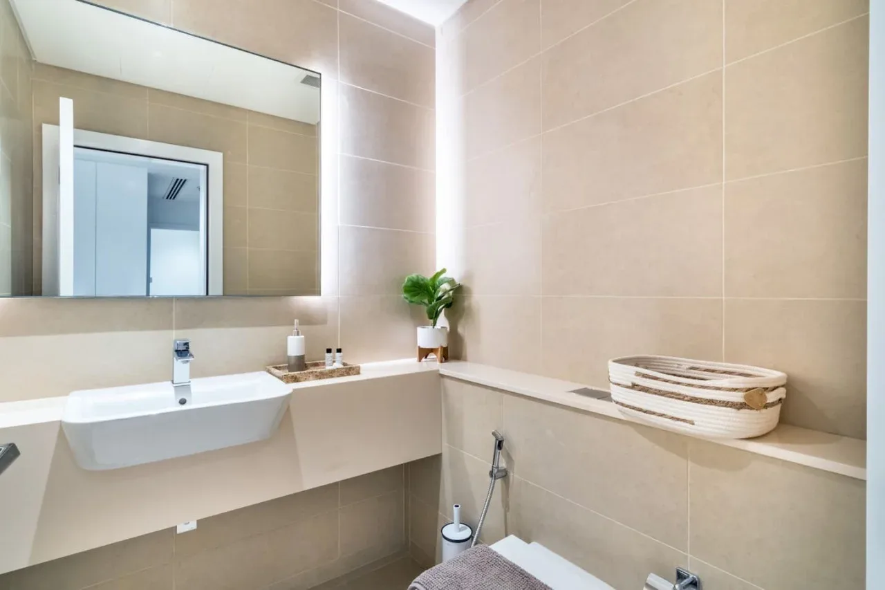 A beige-tiled bathroom with a sink, mirror, and small plant.