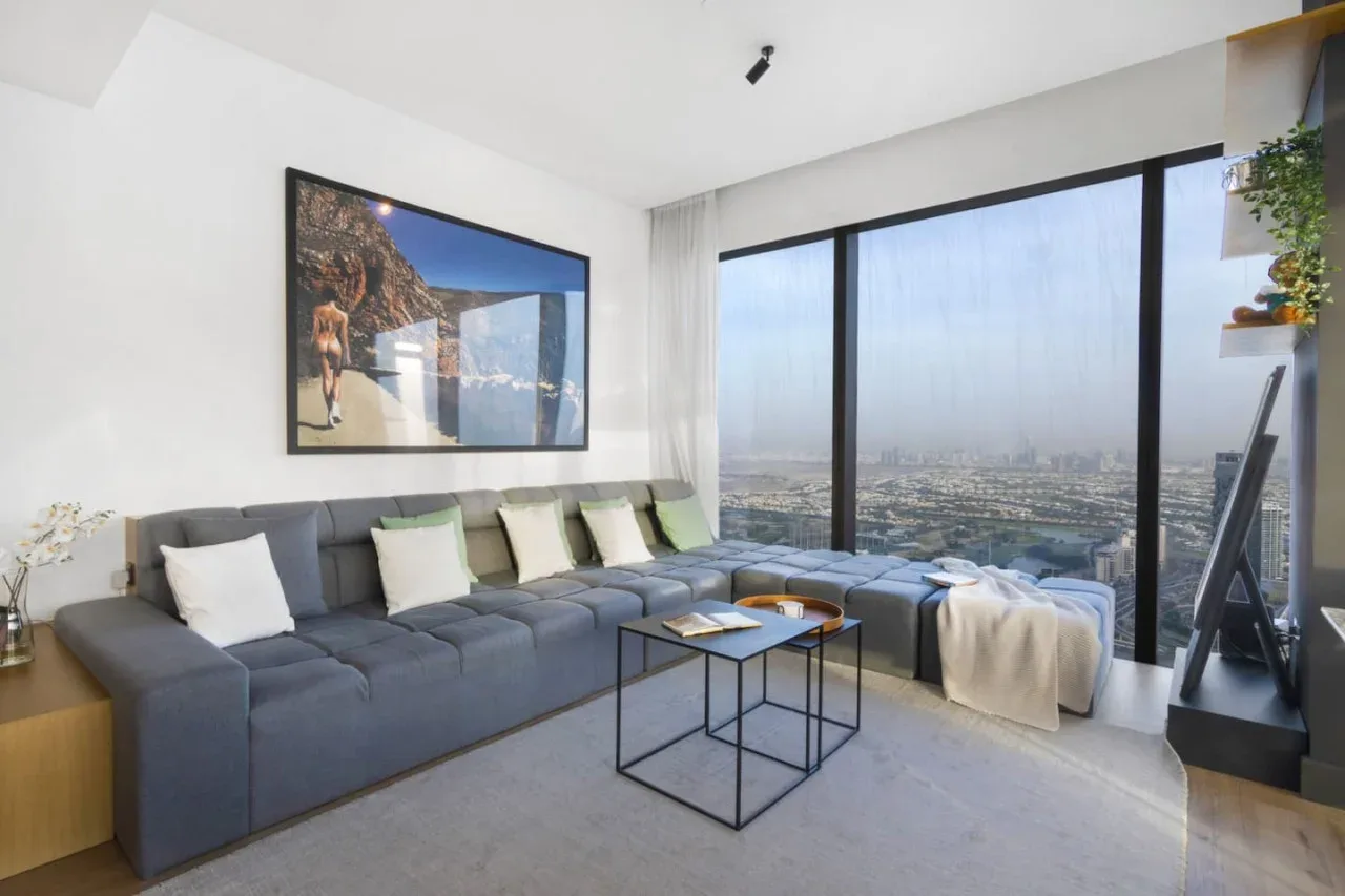 A bright living room with an L-shaped seating area and large windows overlooking the city.