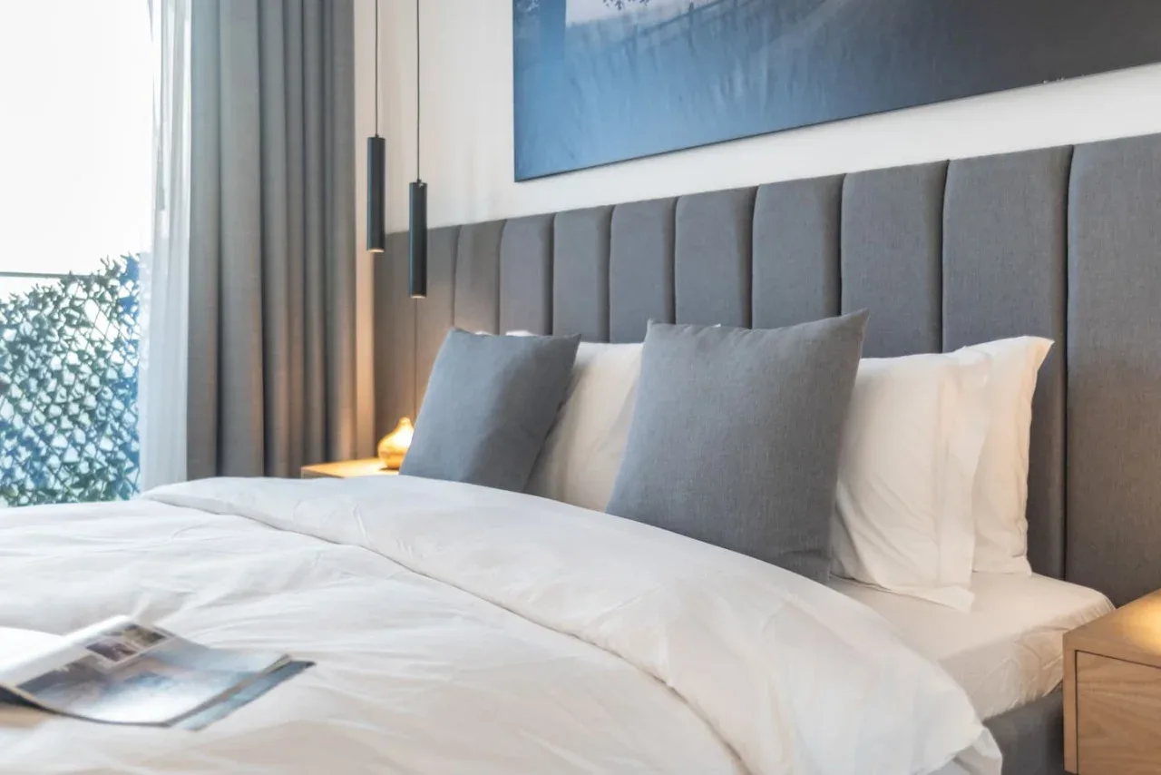 A bedroom with a neatly made bed and gray upholstered headboard.