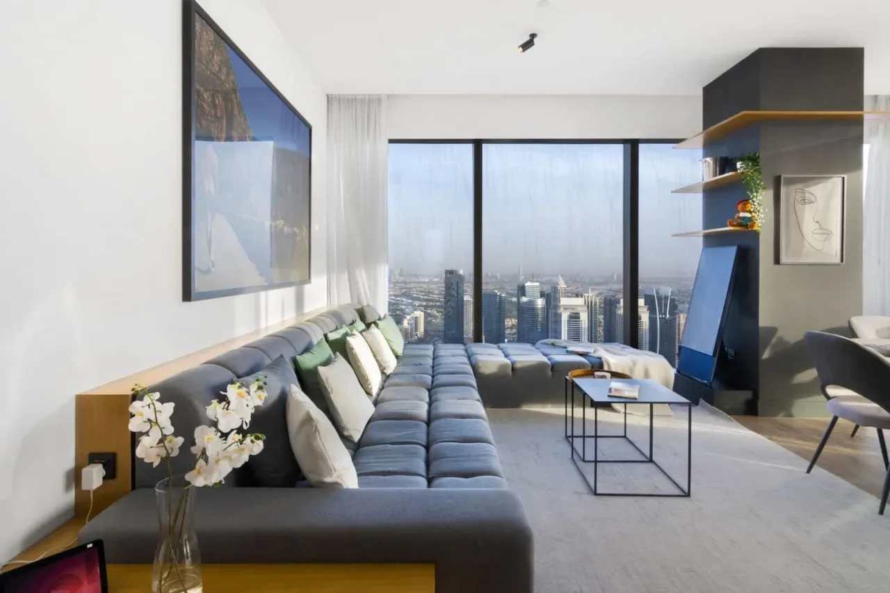 A modern living room with seating and large windows overlooking a city skyline.