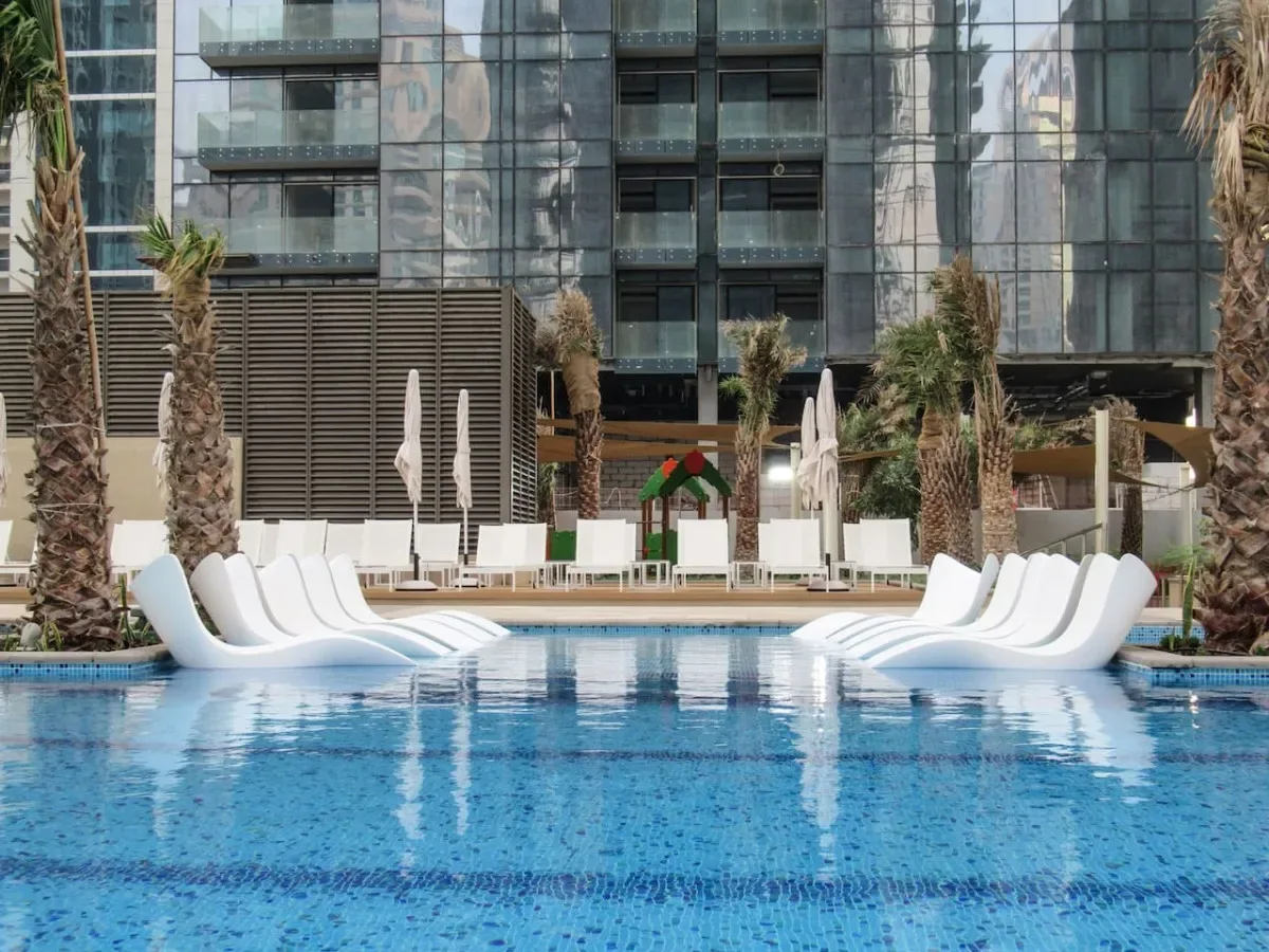 An outdoor swimming pool is lined with white lounge chairs and palm trees.