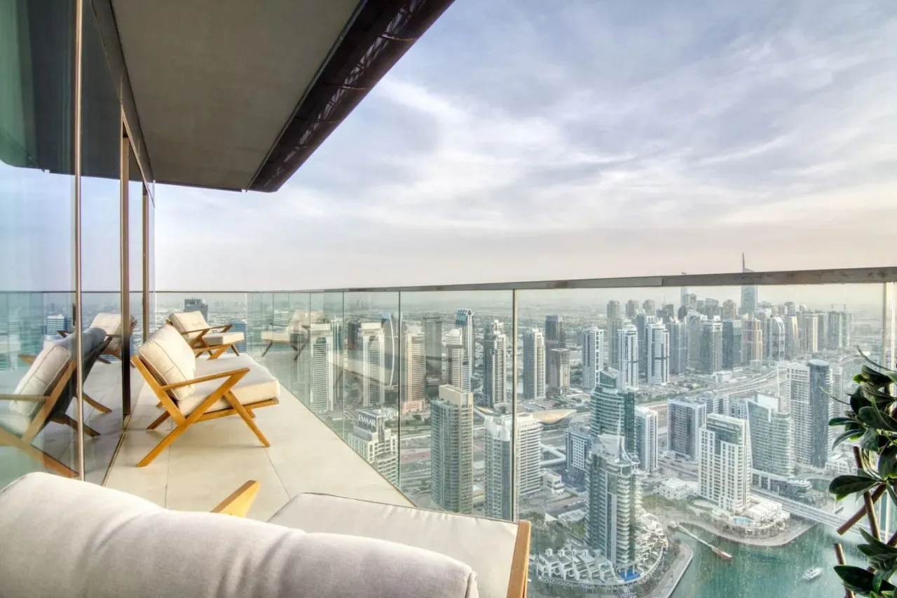 A balcony seating area overlooks a city skyline beyond a glass railing.