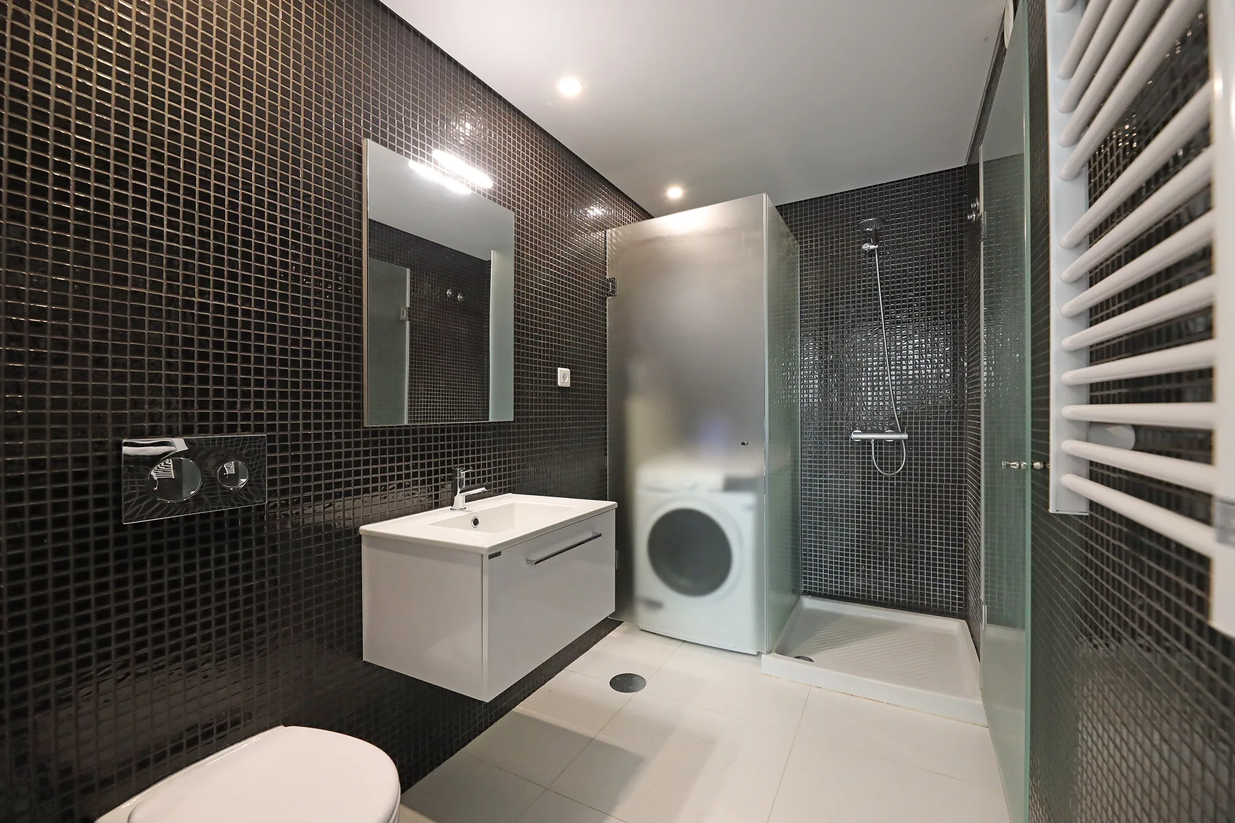 A tiled bathroom with a vanity, washing machine, and shower.