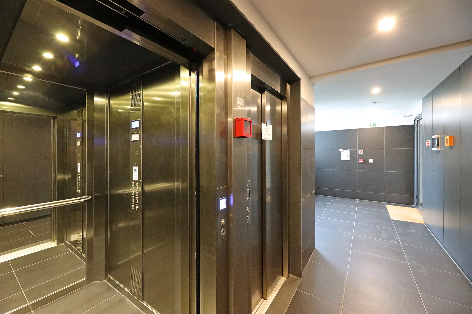 An elevator lobby with reflective elevator doors and a tiled hallway.