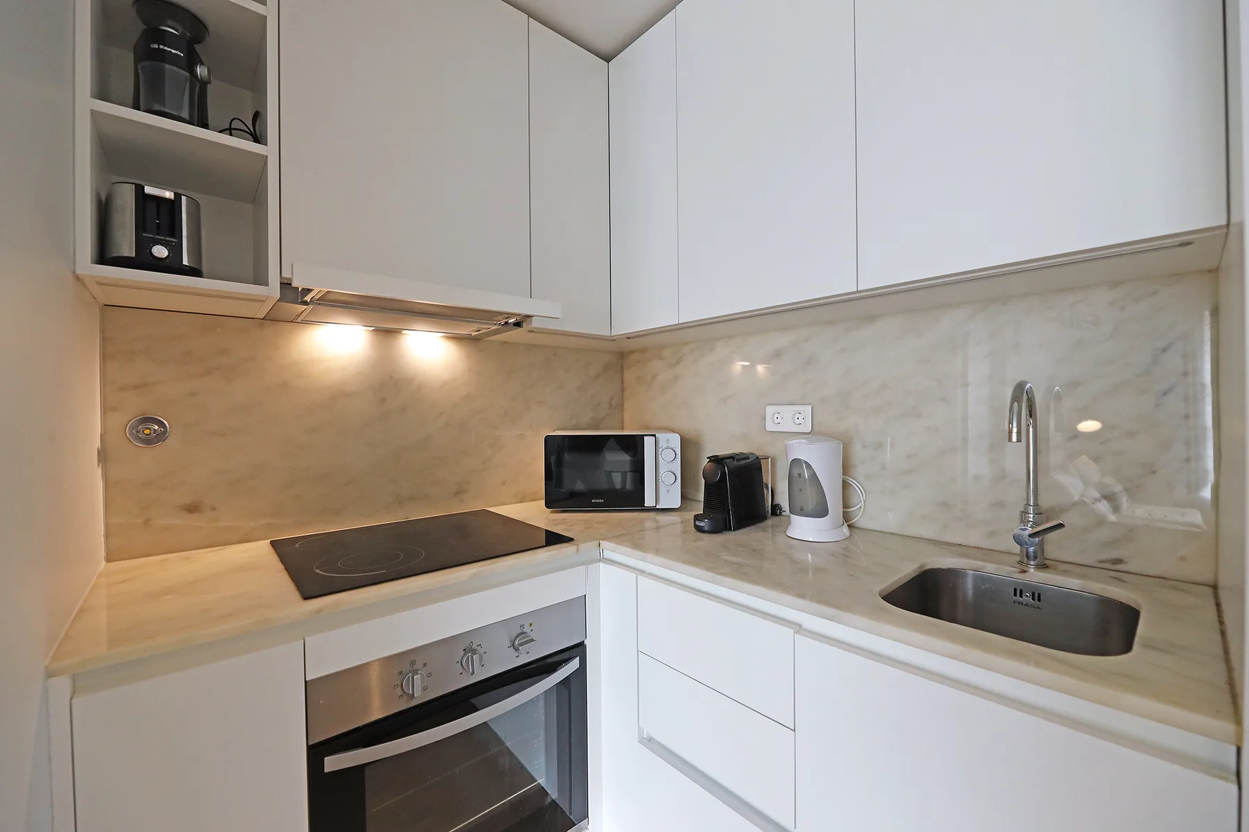 A compact kitchen with white cabinets, a cooktop, and a sink.