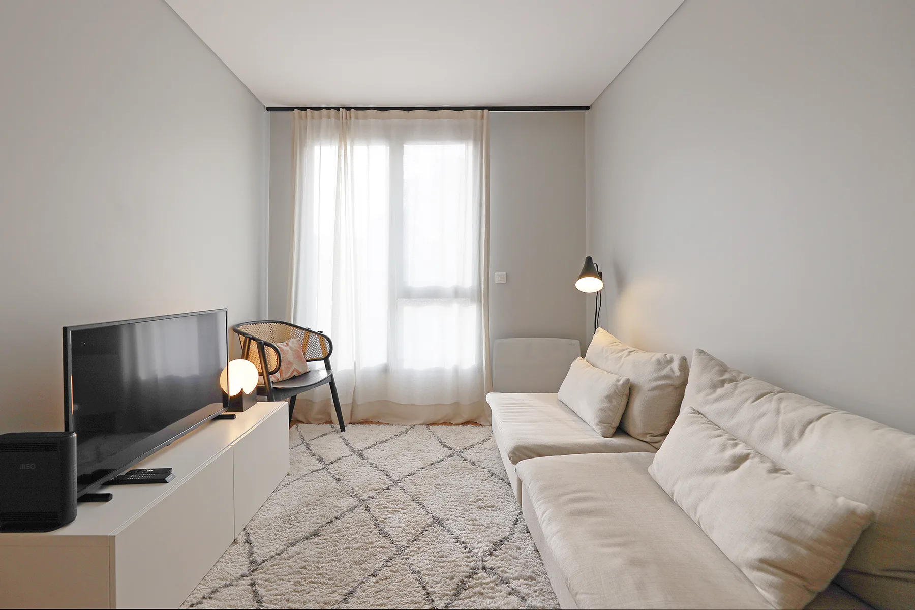 A bright living room with seating, a television, and a large curtained window.