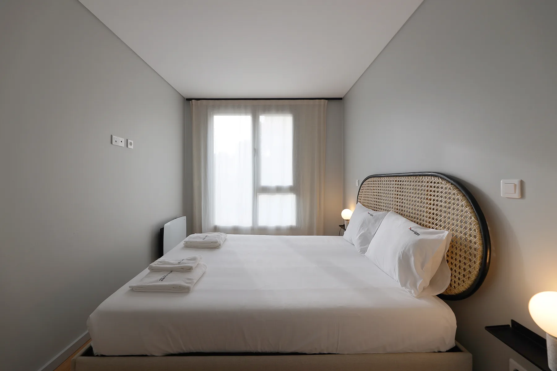 A bright bedroom with a neatly made bed and a window behind it.