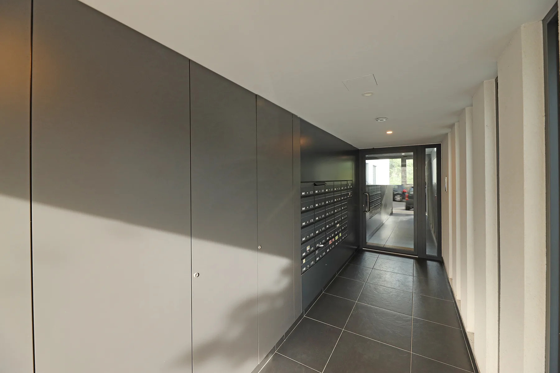 A tiled apartment corridor with a long row of mailboxes along one wall.
