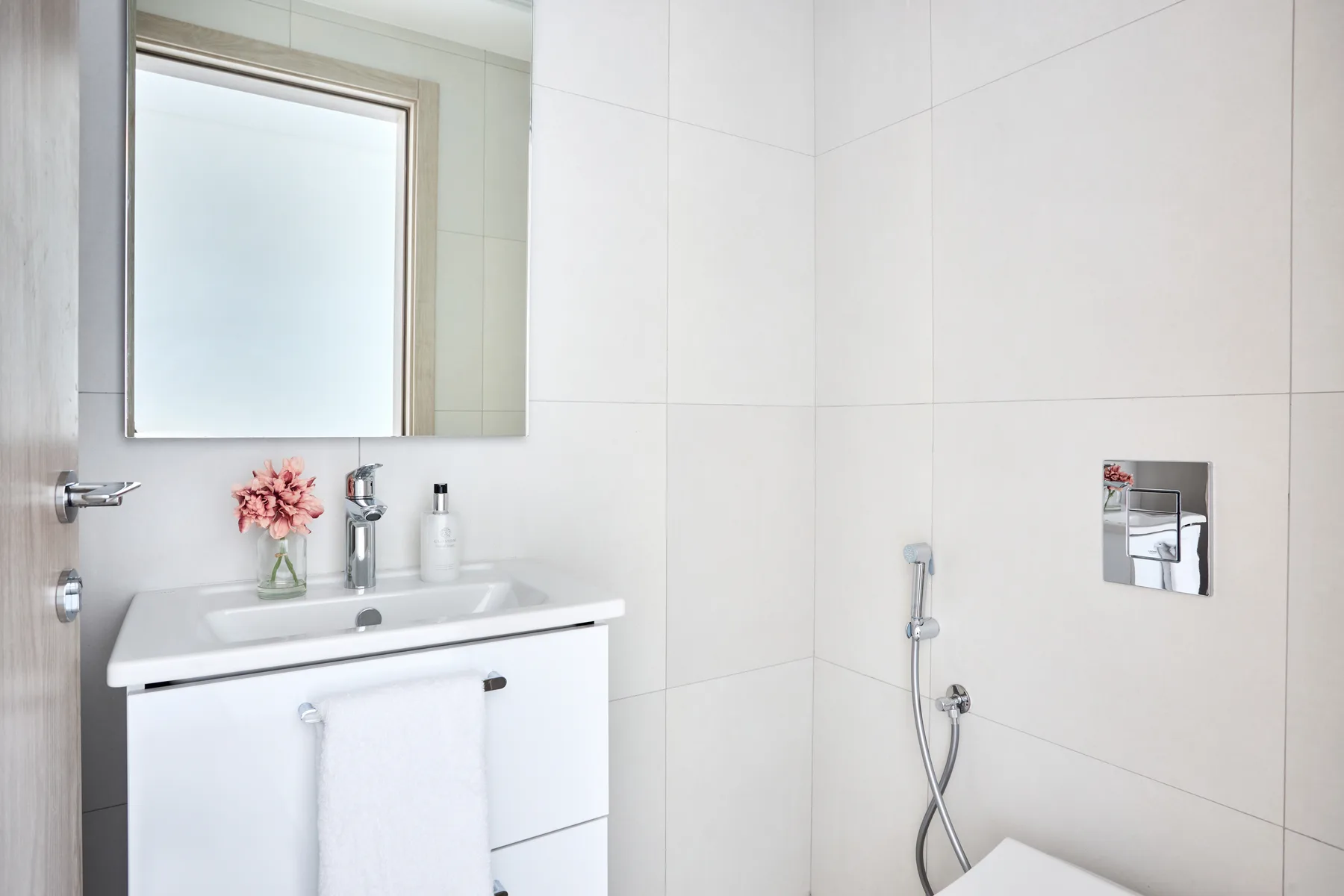 Un baño luminoso con azulejos, lavabo, espejo y controles de ducha en la pared.