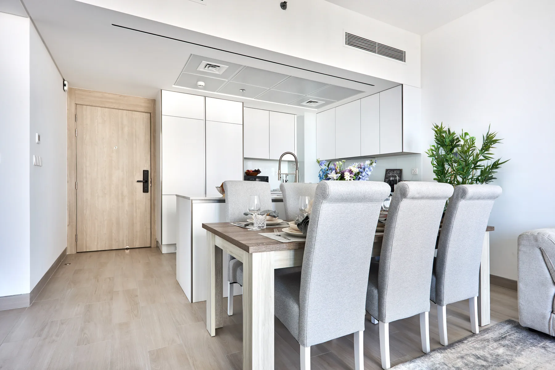 Un comedor luminoso con una mesa, asientos tapizados y una cocina al fondo.