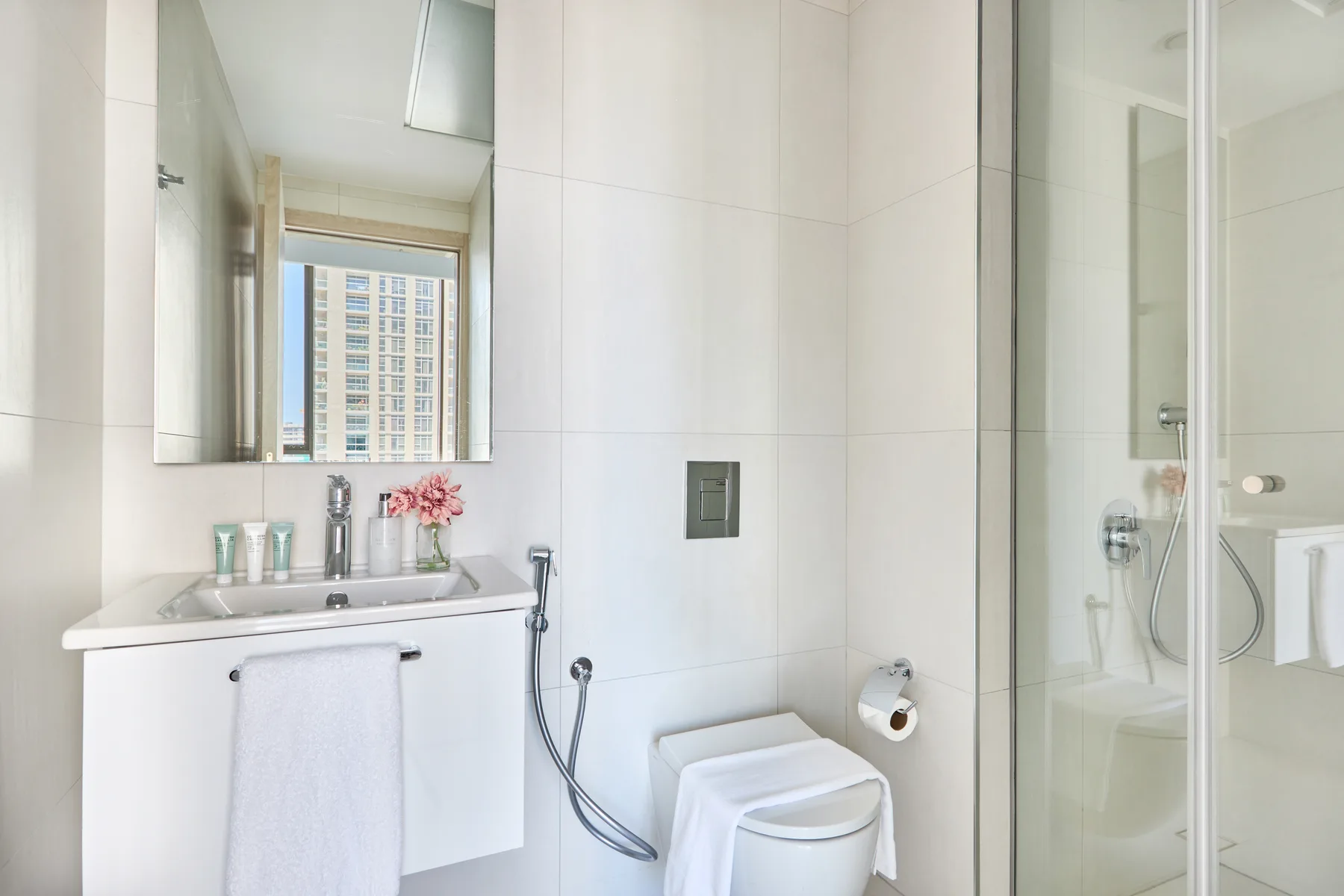 Un baño luminoso con lavabo, espejo, inodoro y ducha de vidrio.