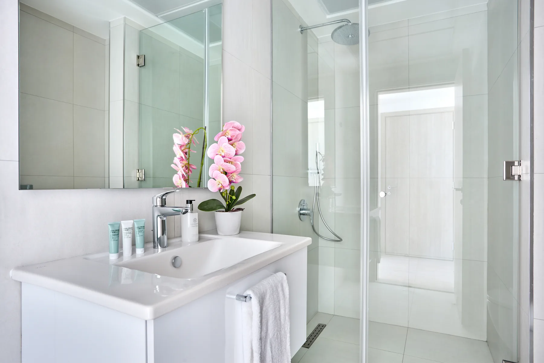Un baño luminoso con lavabo, espejo y ducha de vidrio.