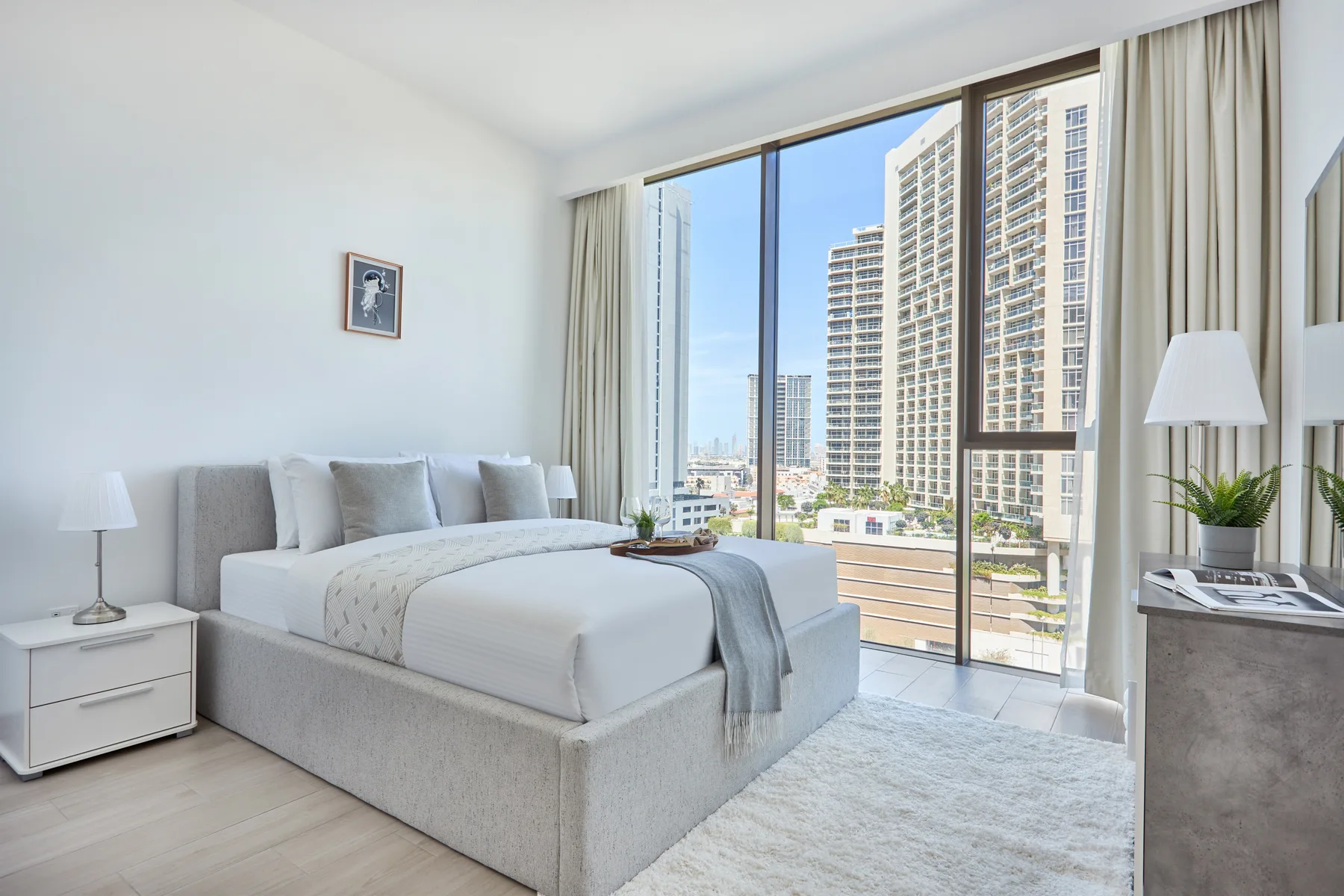 Un dormitorio luminoso con una cama bien tendida junto a ventanas de piso a techo.
