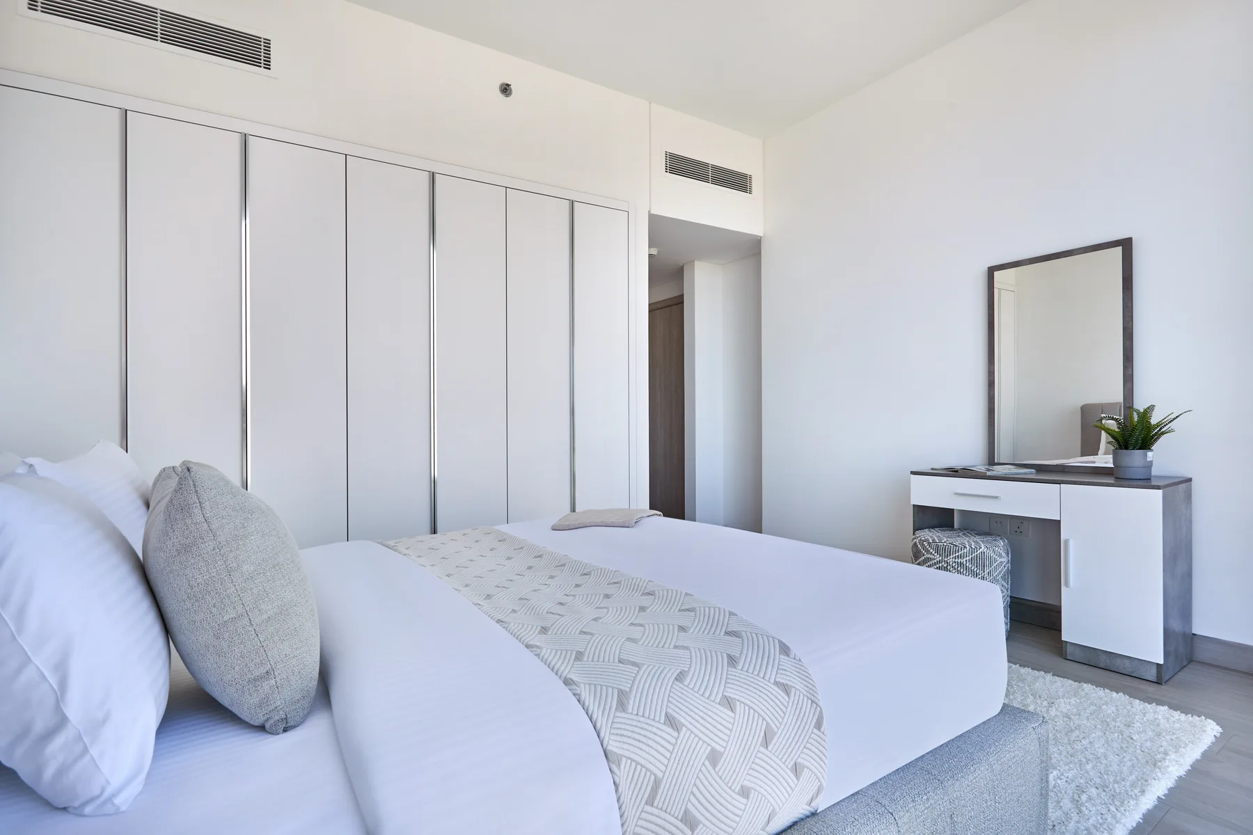 Un dormitorio luminoso con una cama tendida y un tocador.