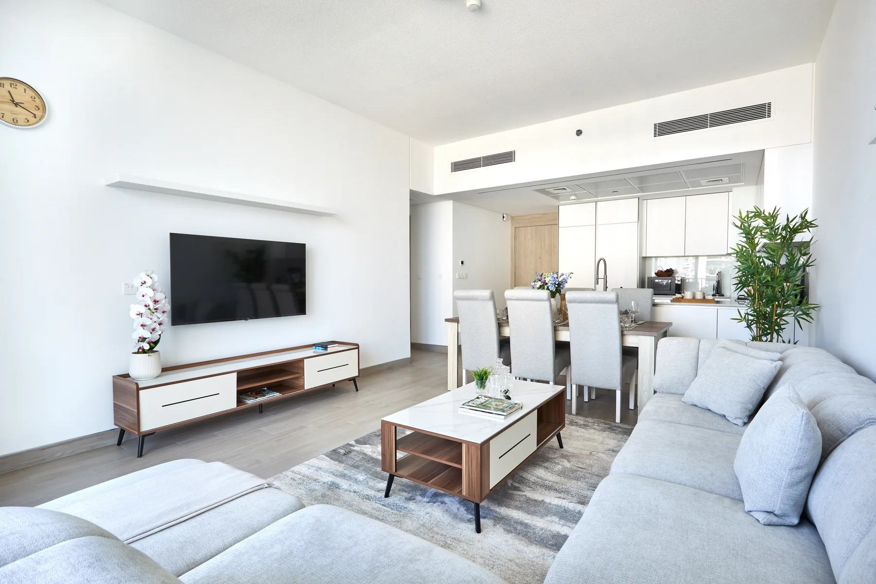 Una sala luminosa con asientos, un televisor y un comedor al fondo.