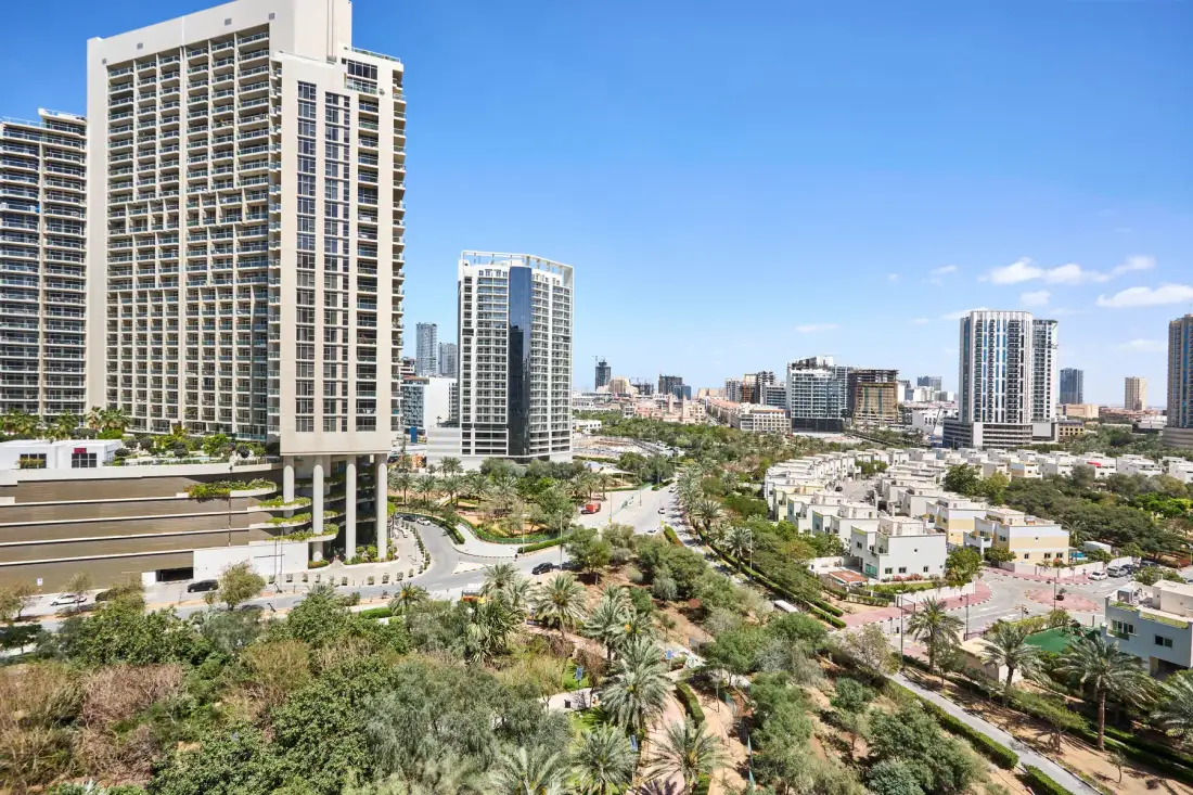 Un paisaje urbano con edificios altos, zonas verdes ajardinadas y viviendas bajas bajo un cielo despejado.