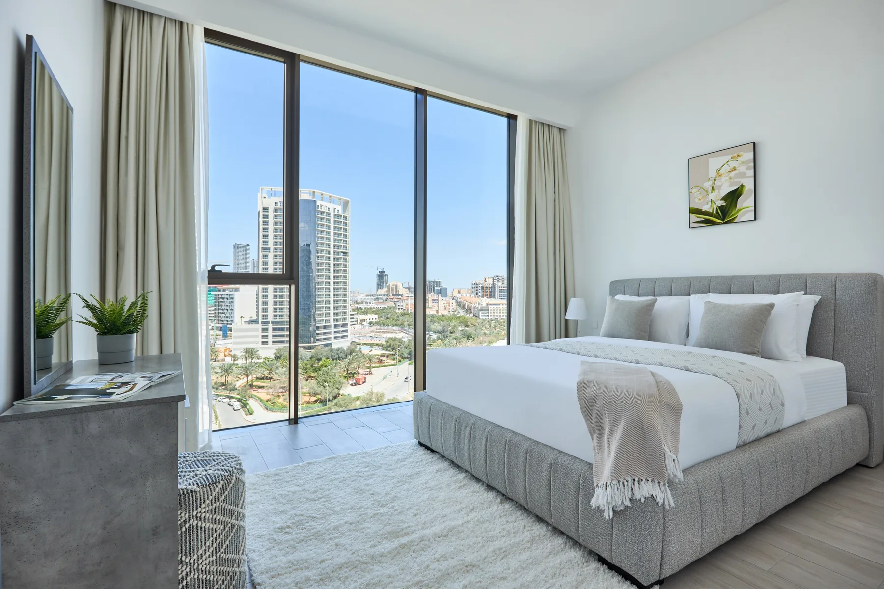 Un dormitorio luminoso con una cama grande junto a ventanales con vistas a la ciudad.