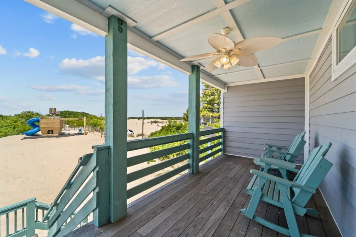 A covered outdoor porch with turquoise seating overlooks a sandy play area.