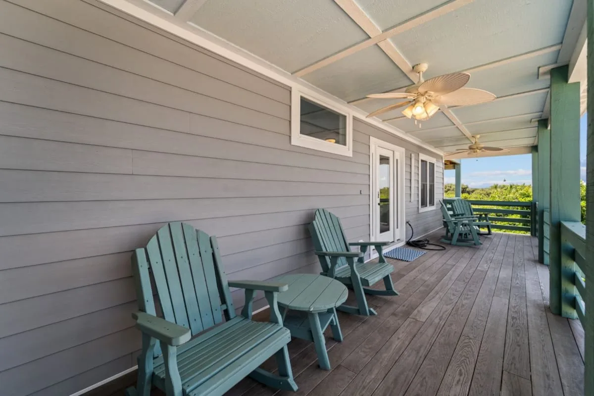 A covered porch with outdoor seating and views of greenery.