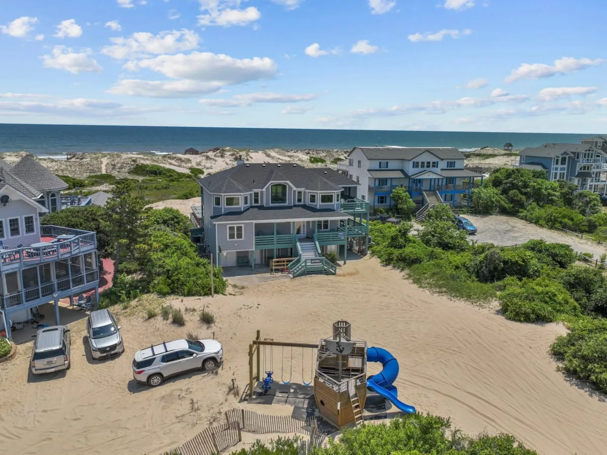 Coastal homes sit beside a sandy beach beneath a blue sky.