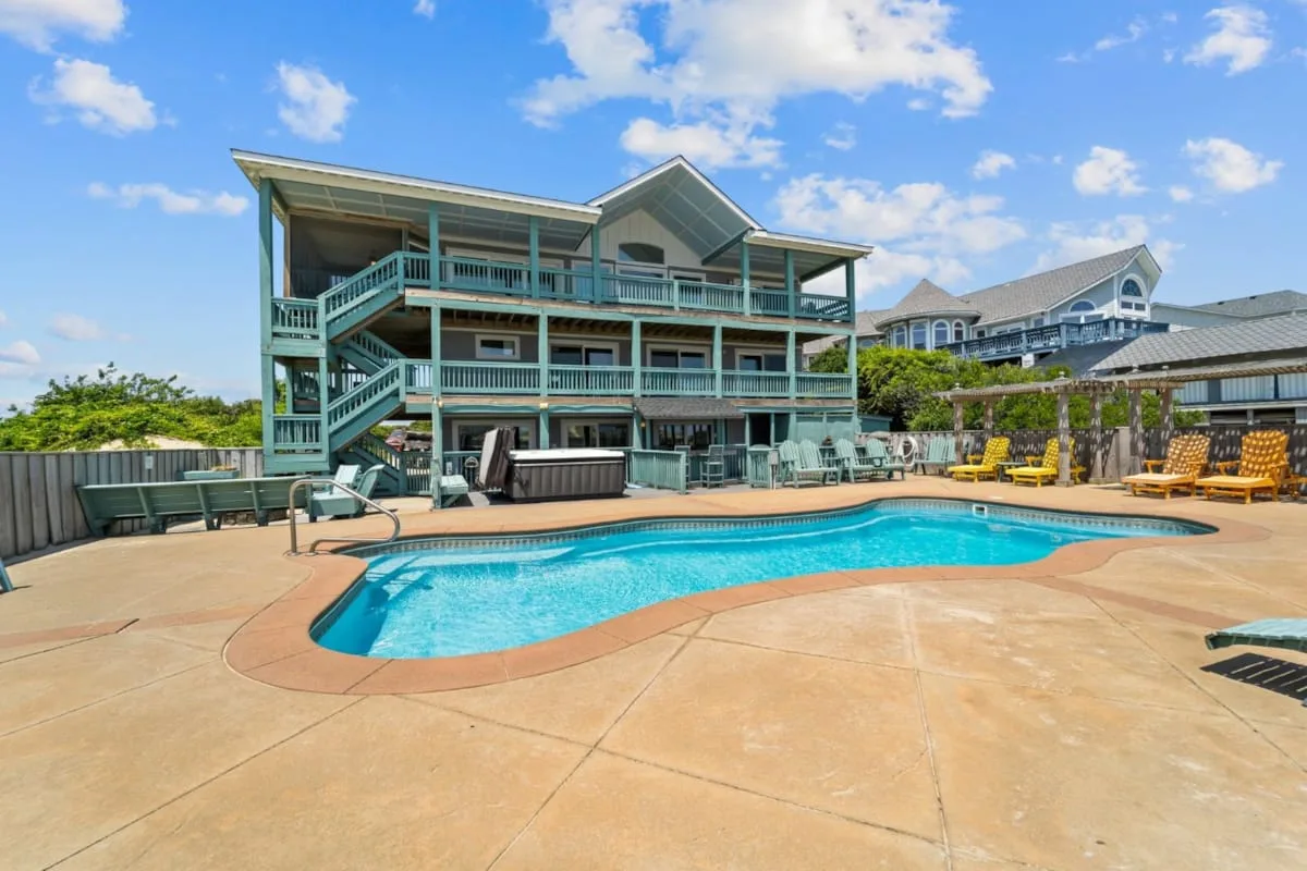An outdoor swimming pool sits in front of a multi-level building and deck seating.