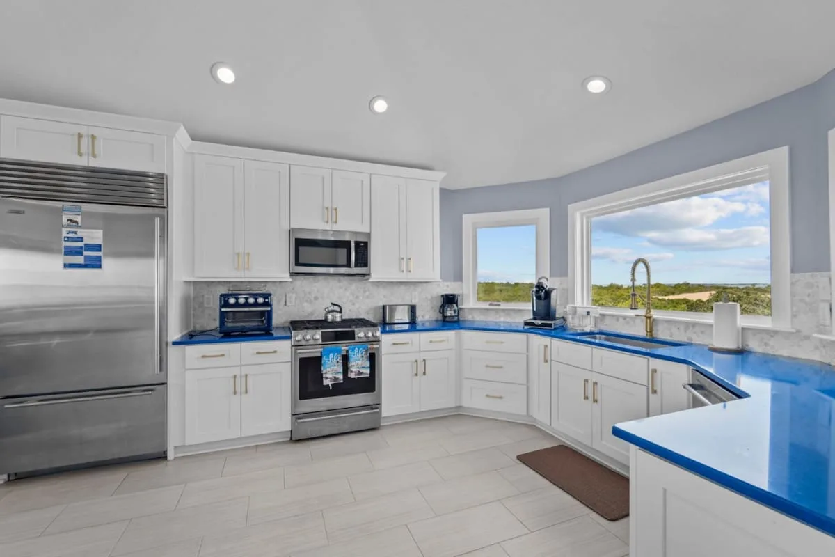 A bright kitchen with white cabinets, stainless steel appliances, and blue countertops.