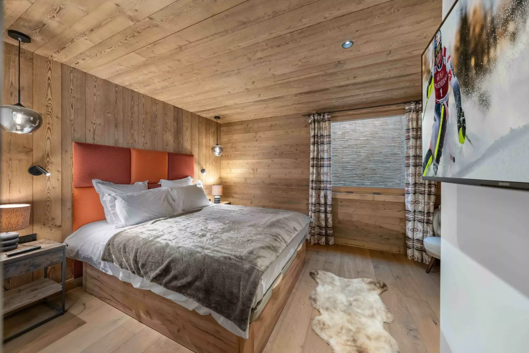 Un dormitorio con paredes de madera, una cama, una ventana y un televisor en la pared.