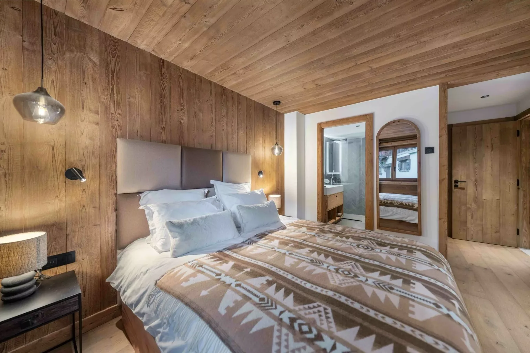 Un dormitorio con una cama grande, ropa de cama estampada y paredes revestidas de madera.