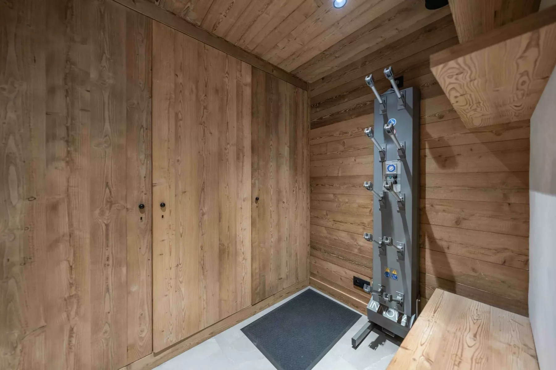 Un cuarto de ducha revestido de madera, con una ducha y una alfombrilla oscura.
