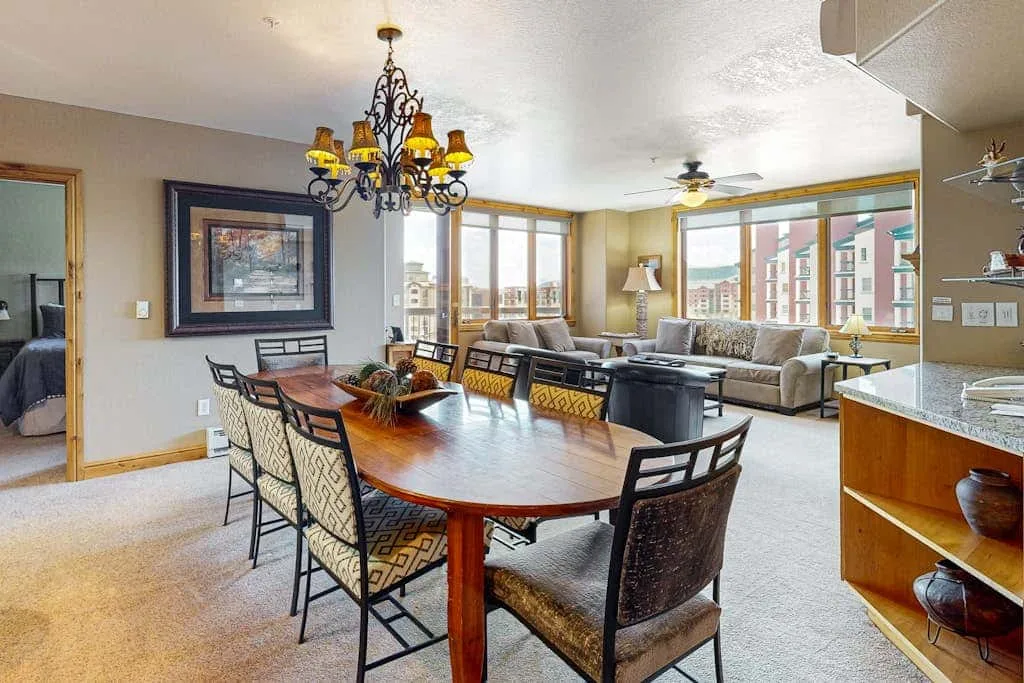 A dining and living area with a wooden table and seating beside large windows.
