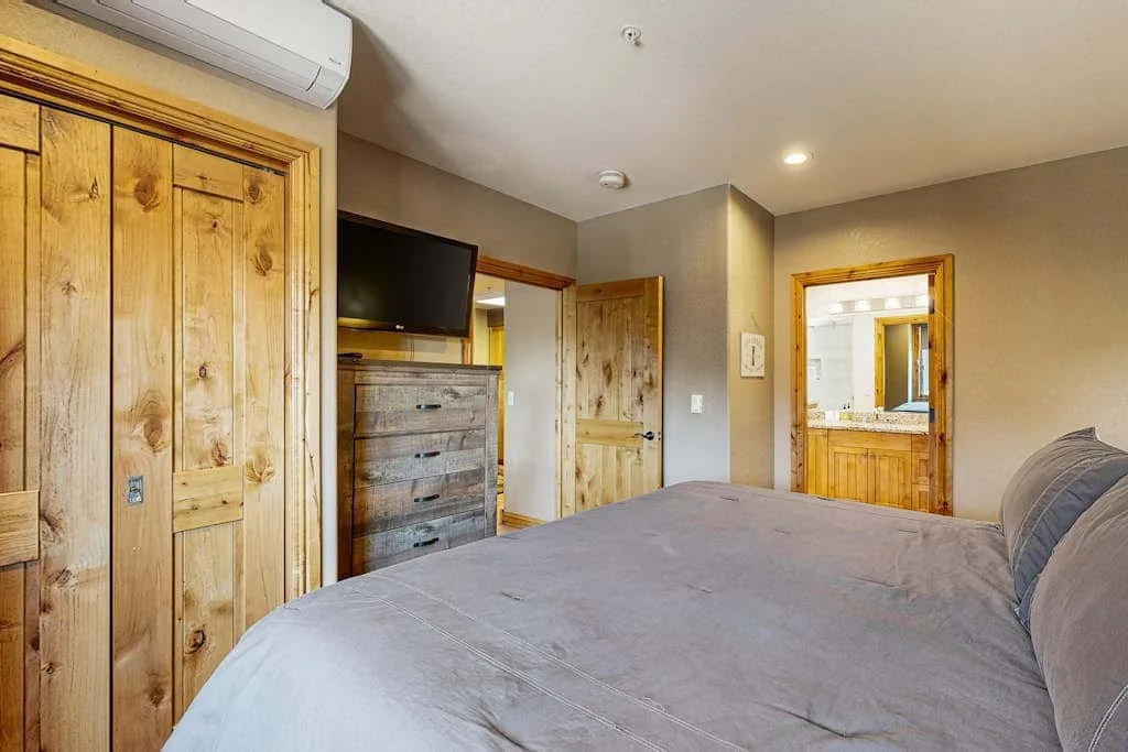 Bedroom with a bed, wooden doors, and a television mounted above a dresser.