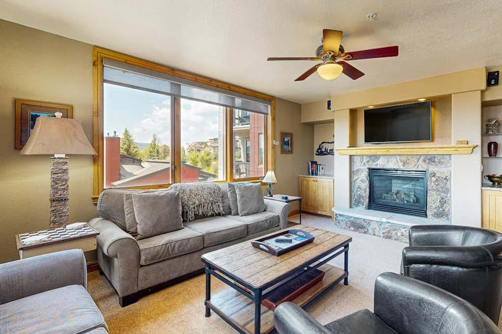 A living room with a sofa, coffee table, and fireplace beside large windows.