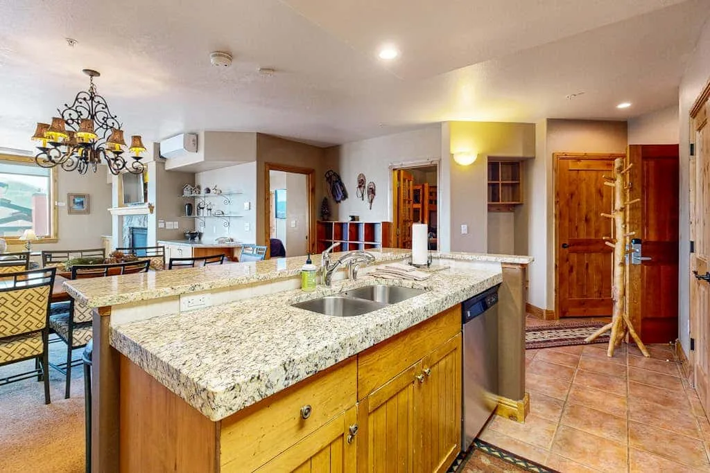A kitchen with a large granite island and sink opens onto a dining area.