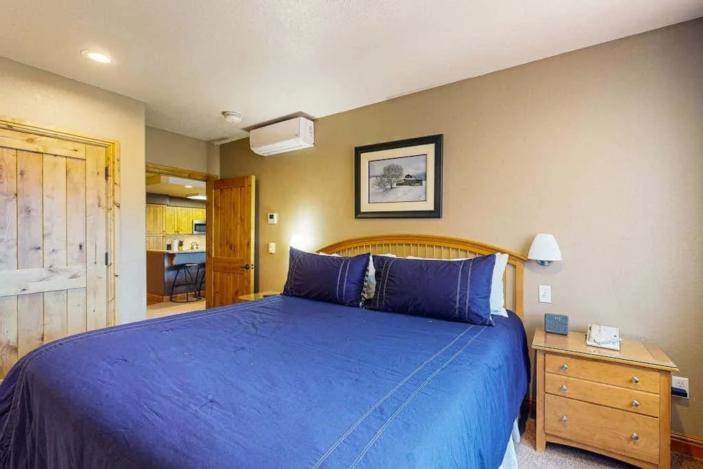 A bedroom with a blue bedspread, wooden headboard, and bedside table.